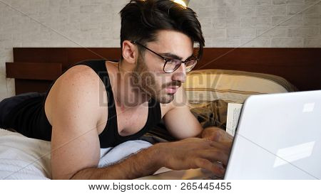Attractive Young Man With Serious Expression, With Laptop On Bed Working On His Start-up Business - 