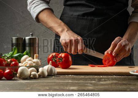The Concept Of Nutrition. The Chef Cuts Tomatoes Close-up, Against The Background Of A Concrete Wall