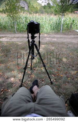 pov photographer in nature taking timelapse photo on pro dslr camera with tripod while sitting in chair and relaxing