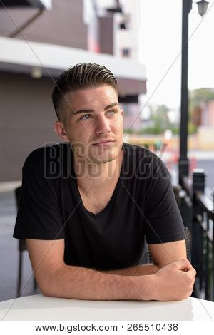 Young Handsome Man Thinking While Leaning On Table Sitting Outsi