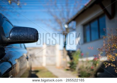 Dirty Rear Mirror On Focus On Parking Car In Front Of A Residentual House.