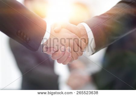 Two businessmen shaking hands with colleagues  on background.