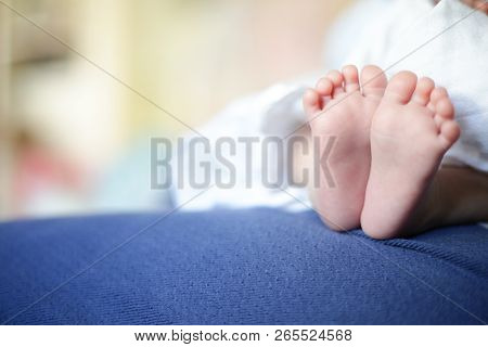 Small Baby Feet Resting On Mother Leg. Soft Smooth Skin Of Infant. Baby Sitting On Mother Lap.