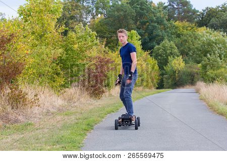 Young European Man Rides Electrical Mountainboard On Road In Nature