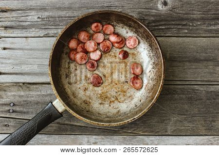 Frying Pan With Fried Pieces Of Sausages On An Old Wooden Table