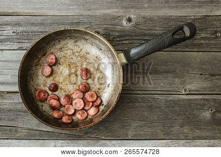 Frying Pan With Fried Pieces Of Sausages On An Old Wooden Table