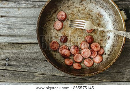 Frying Pan With Fried Pieces Of Sausages On An Old Wooden Table