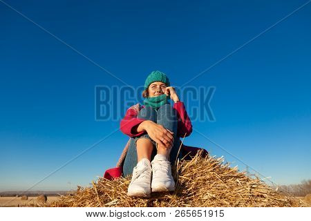 Young Attractive Lady In Blue Knitting Hat And Pink Coat Sitting On Haystack. Smiling Beautiful Hips
