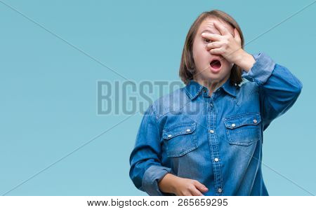 Young adult woman with down syndrome over isolated background peeking in shock covering face and eyes with hand, looking through fingers with embarrassed expression.
