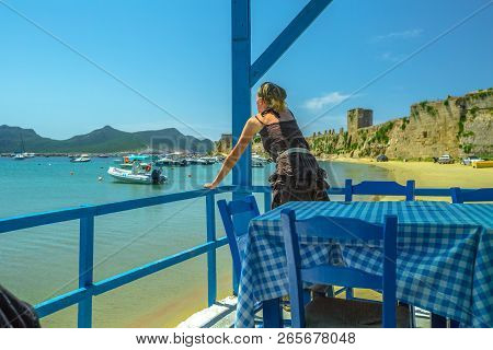 Woman Watching The Sea From A Porch On The Methoni Beach. Female Is Looking Panorama From An Outdoor