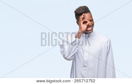 Young arabic african man wearing traditional djellaba over isolated background doing ok gesture with hand smiling, eye looking through fingers with happy face.