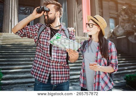 Explorer Stand In Front And Look In Binoculars. He Holds Map In Hand. Femle Tourist Stand Besides Hi
