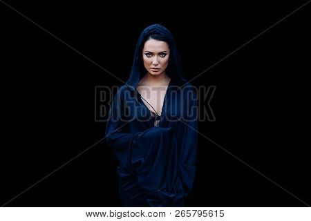Young Beautiful Mysterious Woman With A Black Hair And In The Dark Blue Cloak With Hood At The Black