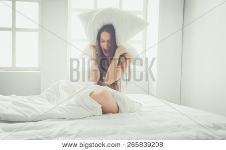 Young caucasian woman covering her head and ears with pillows.