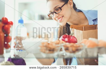 Portrait of female standing near open fridge full of healthy food, vegetables and fruits. Portrait of female