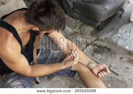 Intravenous Drug User Applying Heroin Syringe Into A Vein. Focus On The Syringe And The Hand Holding