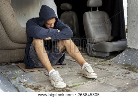 Depressed, Desperate Young Man Sitting On The Building Rooftop Terrace, Wearing Hoodie, Holding Head