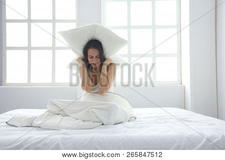 Young caucasian woman covering her head and ears with pillows.