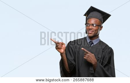 Young graduated african american man over isolated background smiling and looking at the camera pointing with two hands and fingers to the side.