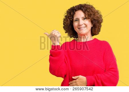 Beautiful middle ager senior woman red winter sweater over isolated background smiling with happy face looking and pointing to the side with thumb up.