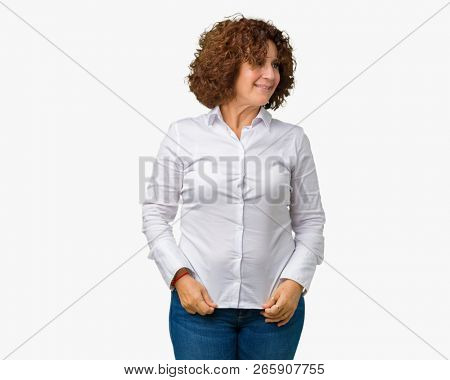 Beautiful middle ager senior businees woman over isolated background looking away to side with smile on face, natural expression. Laughing confident.