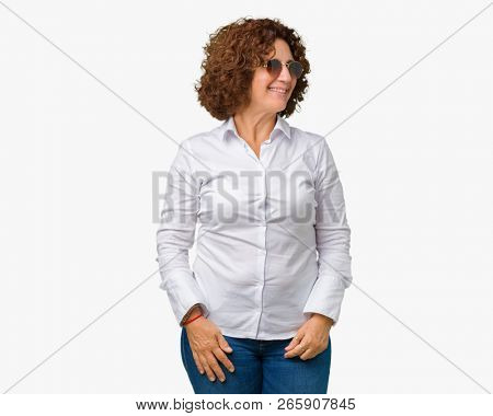 Beautiful middle ager senior business woman wearing sunglasses over isolated background looking away to side with smile on face, natural expression. Laughing confident.