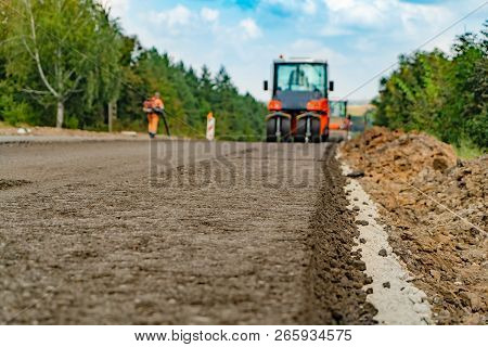 Vibrating Roller Machines Are Compacting Asphalt On The Road. A Man In Working Form Blows Out The Re