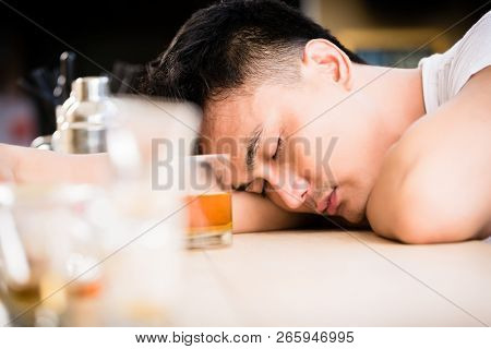 Close-up of a hangover man sleeping in bar with glass of alcohol