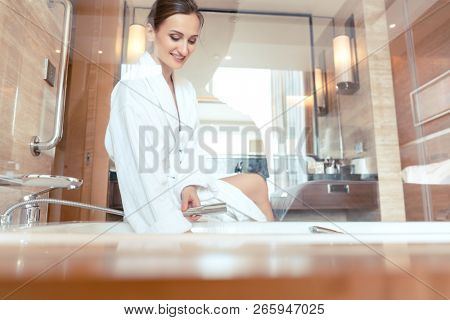 Woman in luxurious hotel bathroom letting water in the bathtub in animation of a relaxing experience 