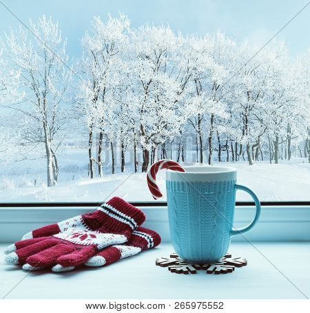 Winter Christmas background. Cup with Christmas candy cane on windowsill and winter trees outdoors. Winter festive composition with Christmas mood, winter Christmas still life