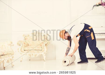Relocating Concept. Man With Beard, Worker In Overalls And Helmet Rolling Carpet, White Background. 