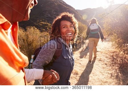 Woman Helping Man On Trail As Group Of Senior Friends Go Hiking In Countryside Together