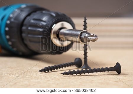 Crosshead Screwdriver And Self-tapping Screws Lie On A Sheet Of Fiberboard. Close-up
