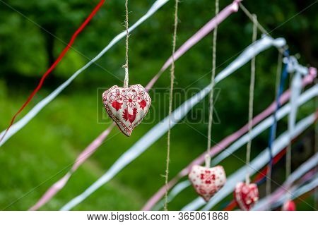Four Handmade Cotton Fabric Heart In Line With Ribbons Hanging On Bast String On Tree On Green Grass