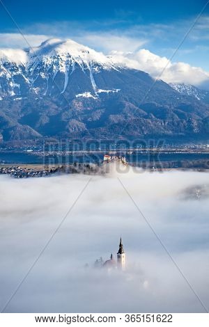 amazing panorama of Lake Bled Blejsko Jezero on a foggy morning with the Pilgrimage Church of the Assumption of Maria on a small island and Bled Castle and Julian Alps in backgroud