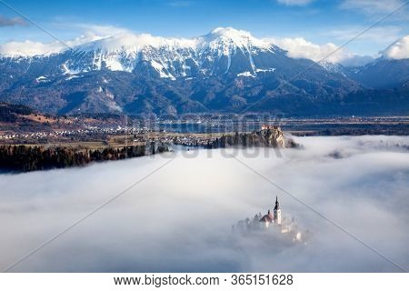 amazing panorama of Lake Bled Blejsko Jezero on a foggy morning with the Pilgrimage Church of the Assumption of Maria on a small island and Bled Castle and Julian Alps in backgroud