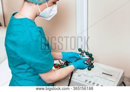 Medical Professional In Surgical Blue Uniform Holding Electrodes Of Ecg Machine, Wearing Gloves And 
