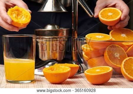 Squeezing an orange with a manual press, close view, making a glass of fresh. Fresh oranges on a wooden table, whole, squeezed and sliced.