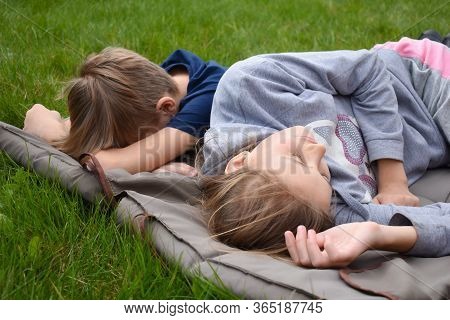 Children Lie On The Mattress Outsite. Boy And Girl Sleeping On The Grass. Summer Holidays In The Fre
