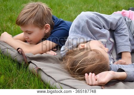 Children Lie On The Mattress Outsite. Boy And Girl Sleeping On The Grass. Summer Holidays In The Fre