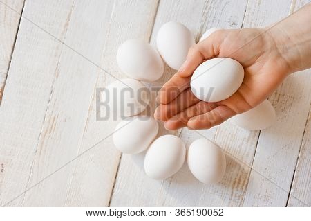 A White Chicken Egg Lying In A Man's Hand, Shot On A White Painted Wooden Surface. Background For Li