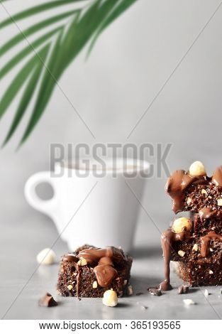 Stack Of A Brownie Pieces With Hazelnut, Palm And Cup On A Grey Table With Gray Background.