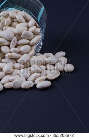 White Beans Spilled Out From Glass Cup. Dark Blued Background.