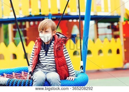 Sad Boy In Face Mask Playing Outdoors. Bored Child At Empty Playground Outside. Coronavirus Quaranti