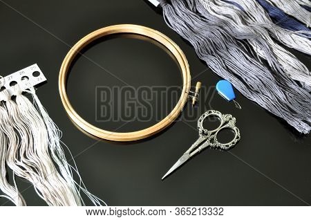 Accessories For Needlework. Hoop, Multi-colored Threads, Scissors, Needle-threader On A Black Backgr