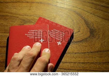 Male Hand Putting Two Swiss Passports On A Wooden Table