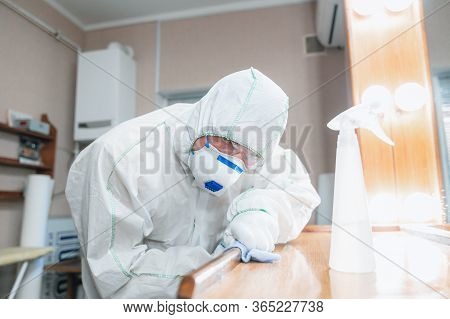 Coronavirus Pandemic. A Disinfector In A Protective Suit And Mask Sprays Disinfectants In House Or O