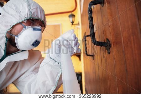 Coronavirus Pandemic. A Disinfector In A Protective Suit And Mask Sprays Disinfectants In House Or O