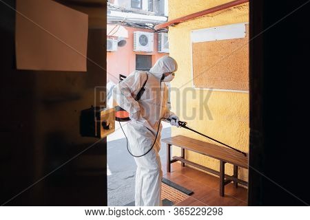 Coronavirus Pandemic. A Disinfector In A Protective Suit And Mask Sprays Disinfectants In House Or O