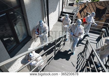 Coronavirus Pandemic. A Disinfectors In A Protective Suit And Mask Spray Disinfectants In House Or O